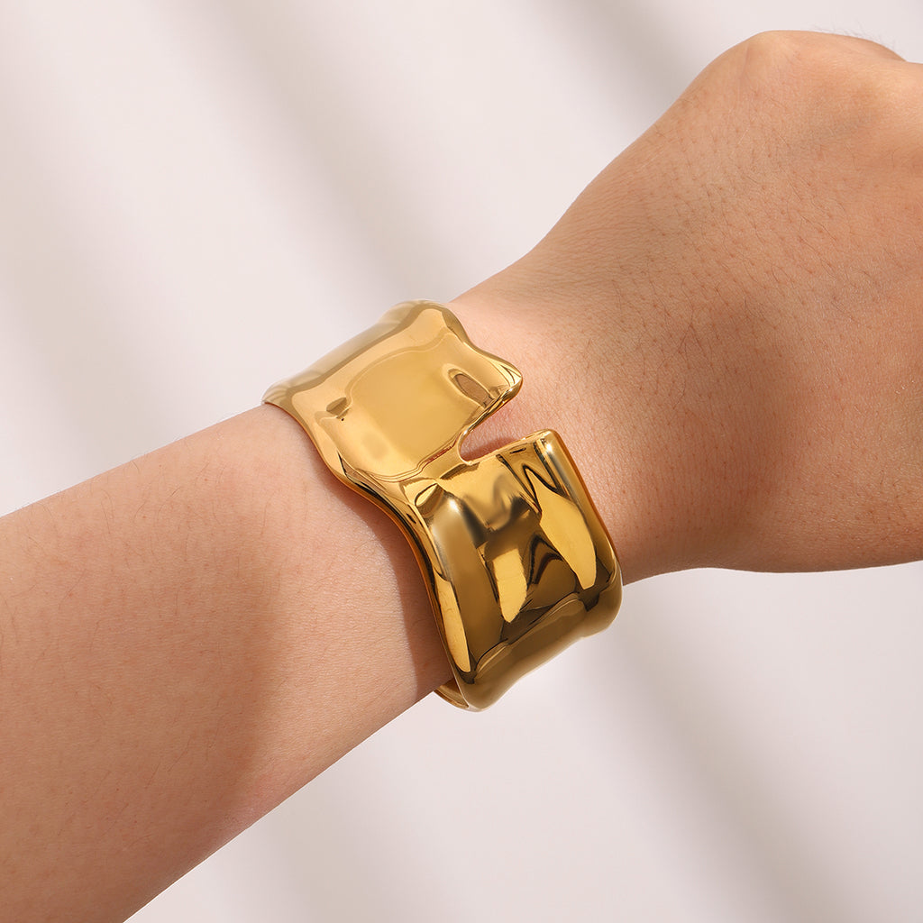 Gold bracelet on a wrist against a plain background