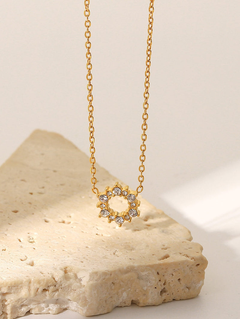 Gold necklace with a circular pendant on a beige stone surface