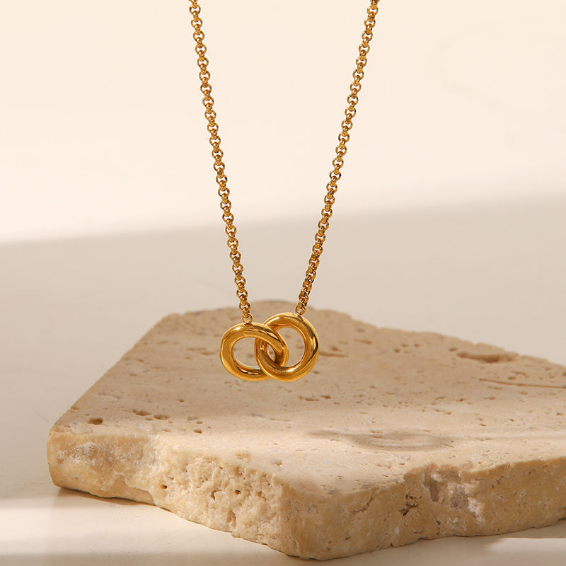 Gold necklace with interlocking rings on a stone surface
