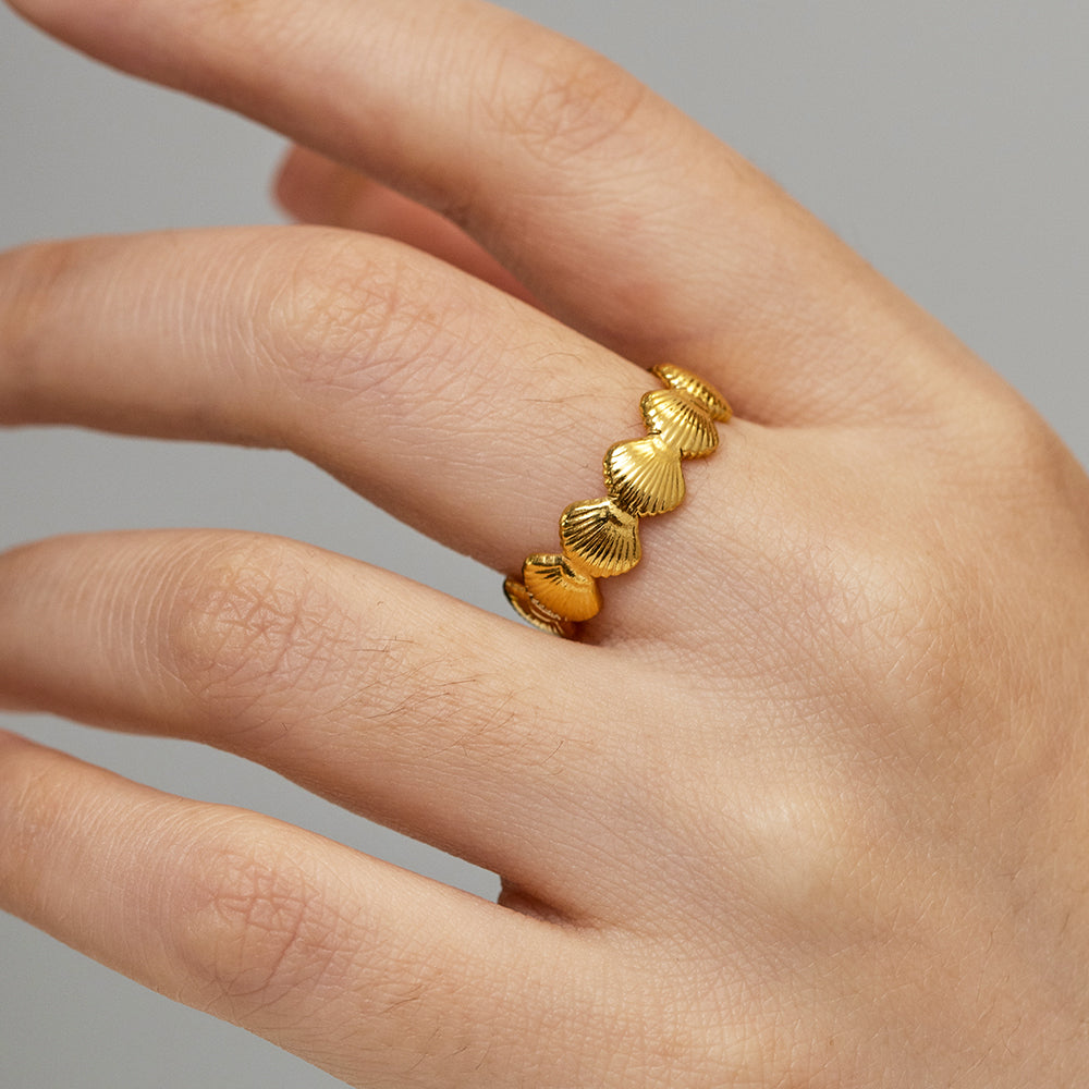 Gold ring with shell design on a hand against a gray background